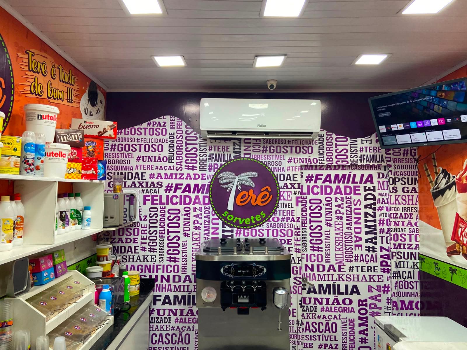 Interior da Terê Sorvetes: o painel roxo com a logo da loja, a máquina de sorvete e as prateleiras de coberturas